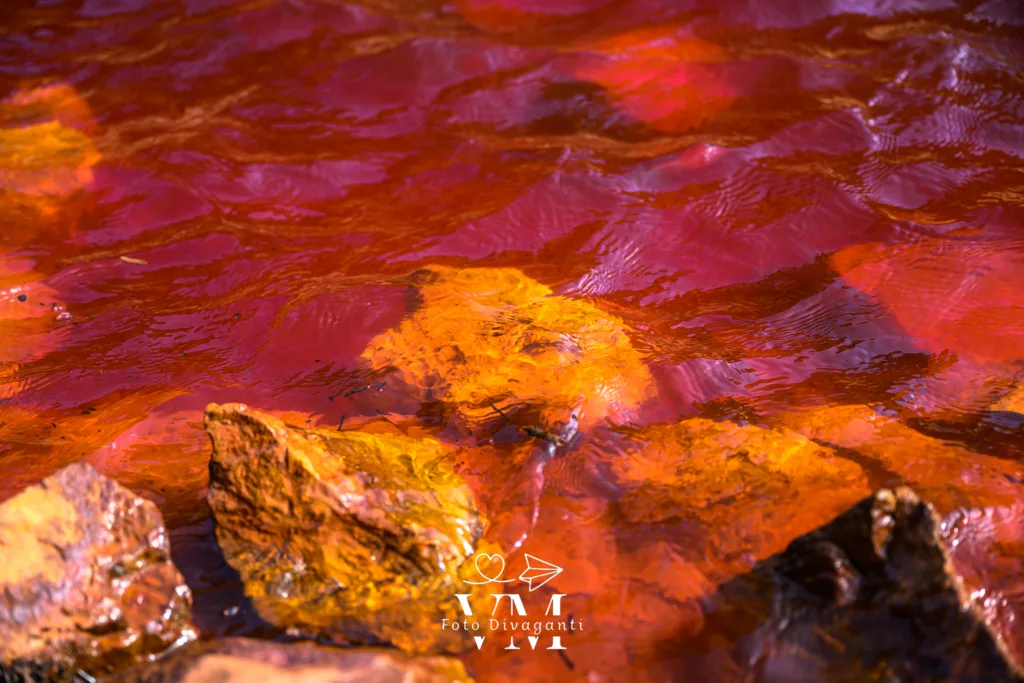 Acqua rossa con riflessi e rocce arancioni sommerse visibili sotto la superficie.