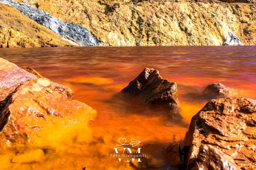 Lago con acqua arancione e rossastra circondato da rocce gialle e marroni.