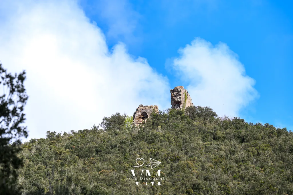 Ruderi in pietra sulla cima di una collina verde con cielo azzurro e nuvole sullo sfondo